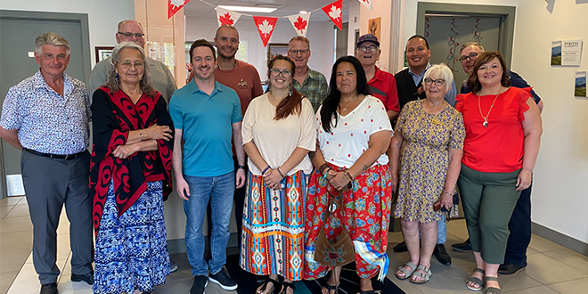 A group of 15 people standing together. They are smiling. There are Canadian flag decorations behind them. 
